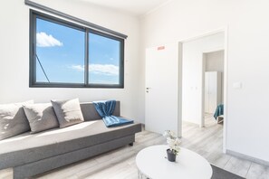 A modern living room with a grey sofa, a blue throw, and a white coffee table with a potted orchid.