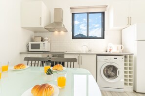 A modern kitchen with a dining table, chairs, a microwave, a coffee maker, a washing machine, and a window with a view. - Casa da Avó by Atlantic Holiday (Caniçal)
