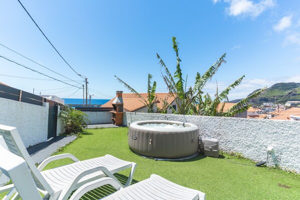 A backyard with a hot tub, white chairs, and a view of the sea.