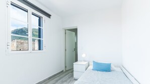 Une chambre à coucher avec un lit, une table de chevet, une lampe et une fenêtre donnant sur un pont et des collines.