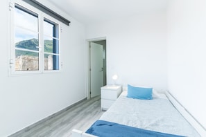 A bedroom with a bed, a nightstand, a lamp, and a window with a view of a bridge and hills. - Casa da Avó 2 by Atlantic Holiday (Caniçal)