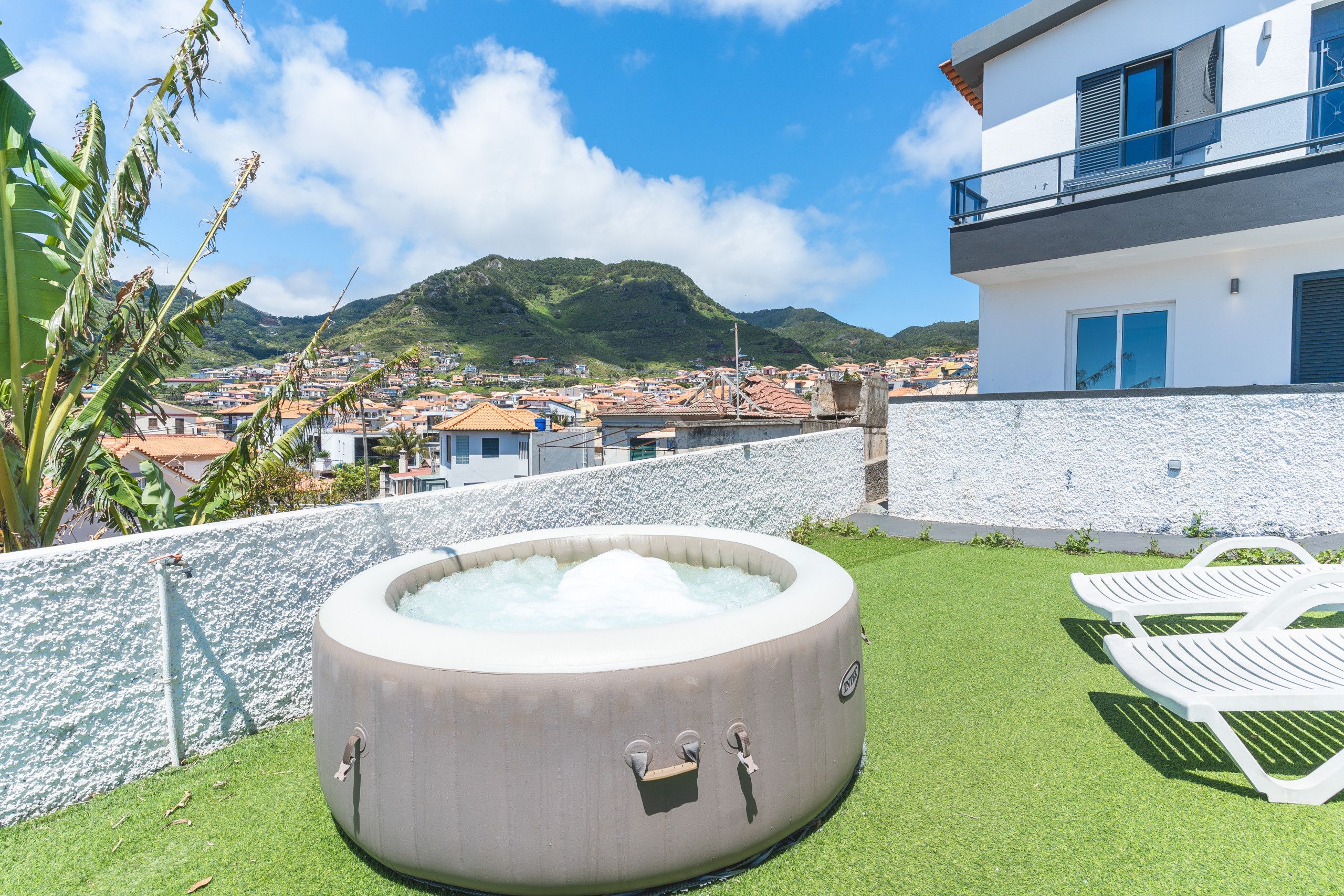A hot tub on a grassy lawn with a view of a hillside town.