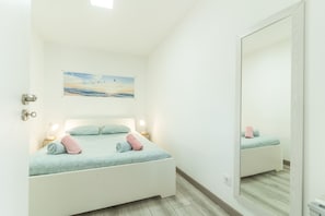 A bedroom with a bed, pillows, a nightstand, a lamp, a painting, and a mirror. - Casa da Avó 2 by Atlantic Holiday (Caniçal)