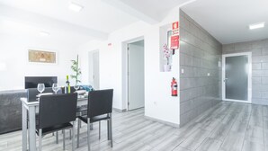 Une chambre d’hôtel moderne dotée d’un coin repas, d’un extincteur fixé au mur et d’une porte donnant sur une autre chambre.