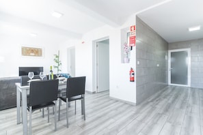 A modern hotel room with a dining area, a fire extinguisher mounted on the wall, and a door leading to another room. - Casa da Avó 2 by Atlantic Holiday (Caniçal)