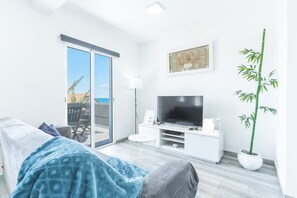 A modern living room with a sofa, a flat-screen TV, a dining table, and a large potted plant.