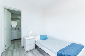 A small, single-bed room with a bedside table, a mirror, and a nightstand.