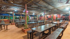 A spacious indoor dining area with multiple wooden tables and benches, brick walls, and ceiling fans. - Treebo Rock Valley (Ponda)