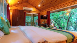 A wooden cabin bedroom with a bed, a TV, and a view of trees. - Treebo Rock Valley (Ponda)