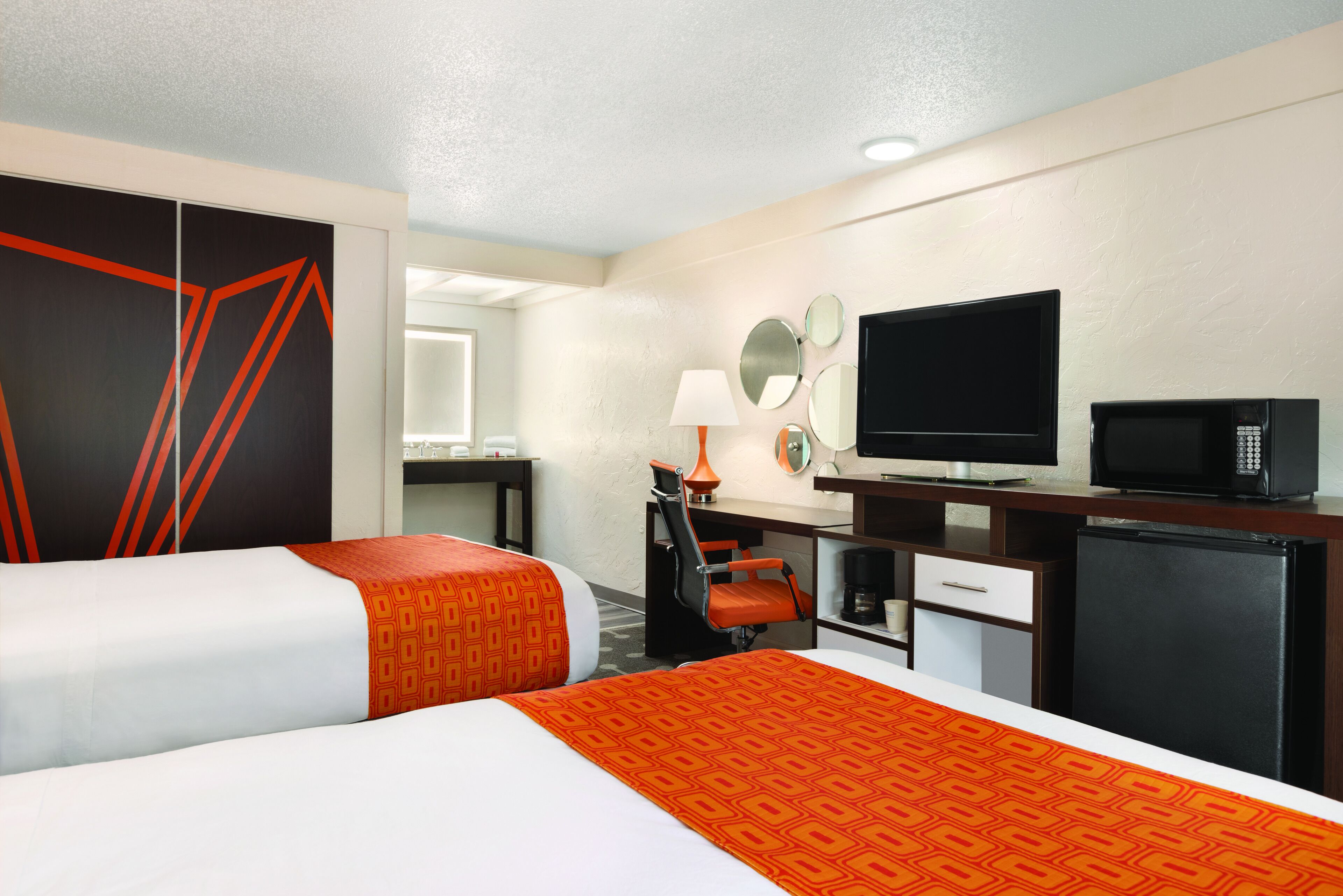 A hotel room with two beds, a desk with a TV, a microwave, and a refrigerator.