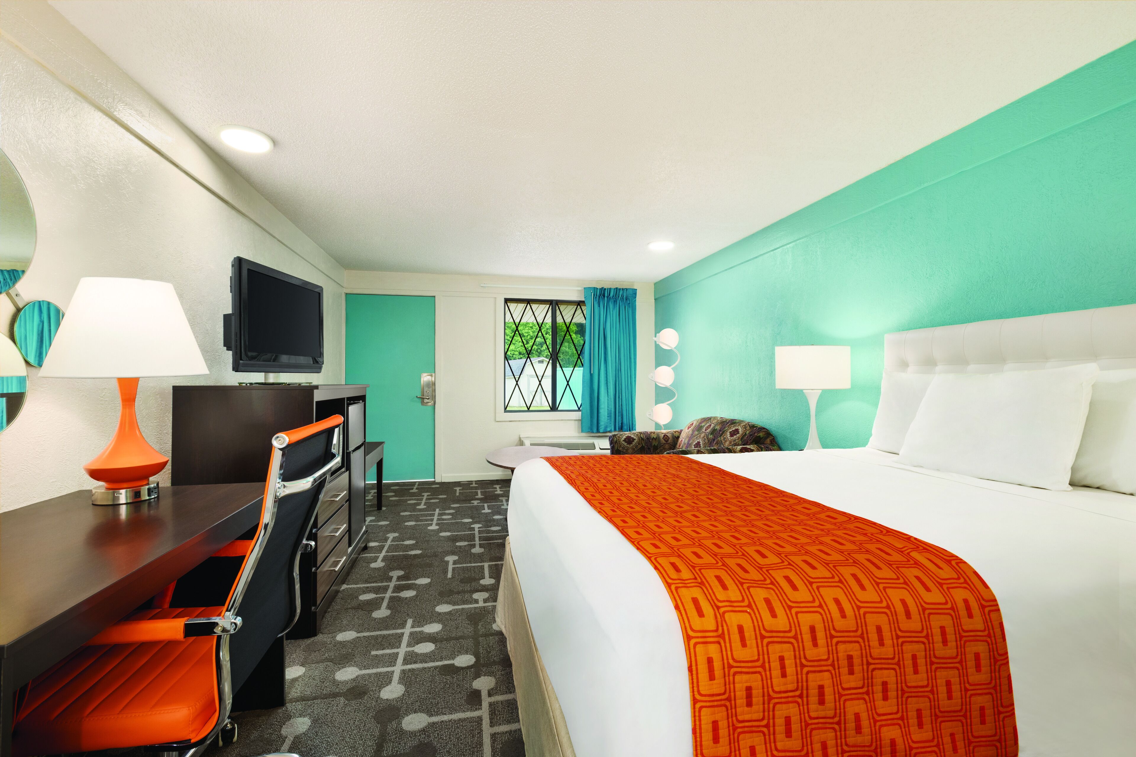 A hotel room with a bed, desk, chair, television, and a window with curtains.