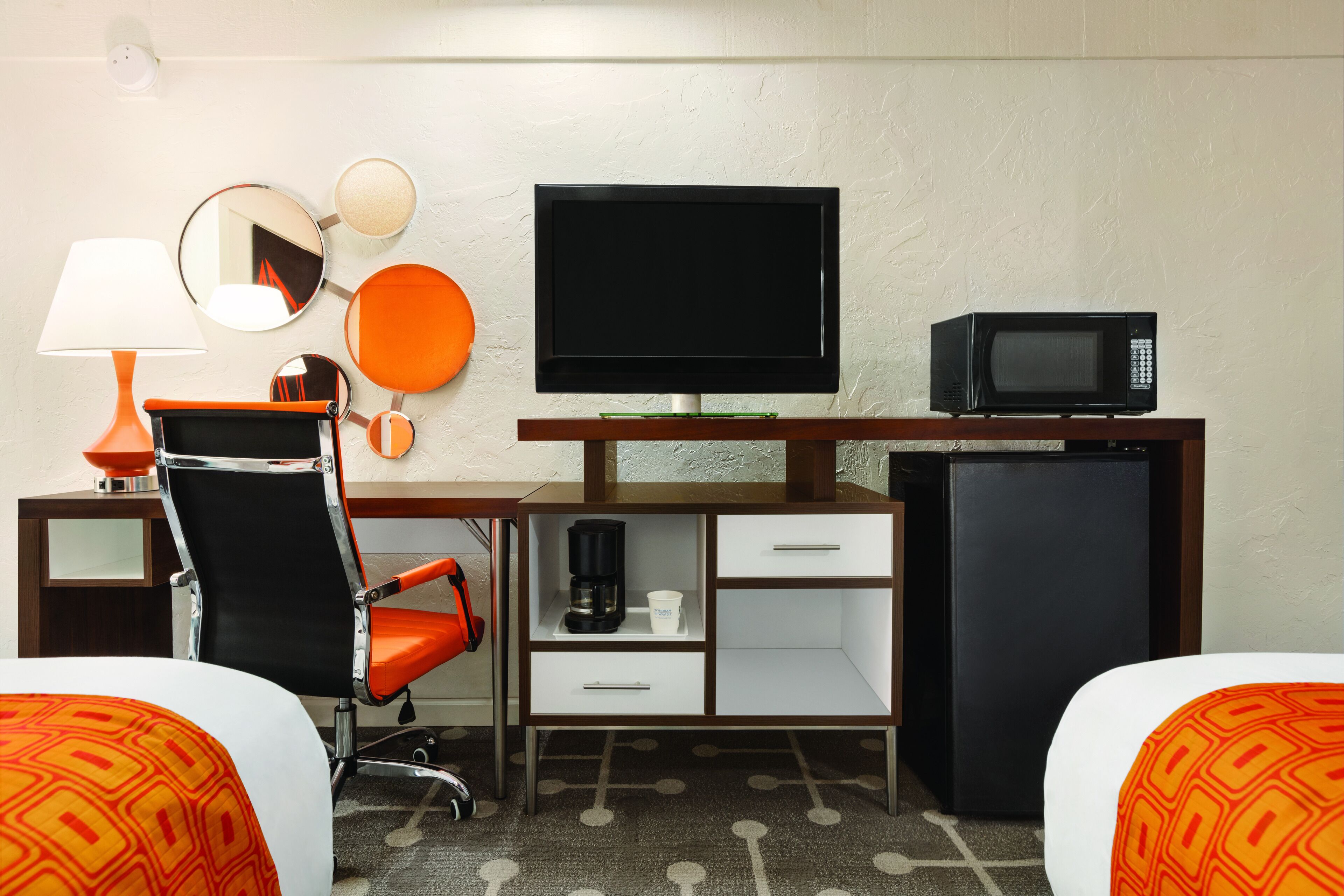 Une chambre d’hôtel équipée d’un lit, d’un bureau avec un ordinateur, d’une télévision, d’un four à micro-ondes, d’une machine à café et d’une chaise.