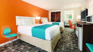 Ein Hotelzimmer mit einem großen Bett, zwei Nachttischen, einem Schreibtisch mit Computer, einem Sessel und einem Fernseher.
