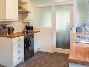 A compact kitchen with white cabinets, a stove, and a wooden countertop. - 2 bedroom accommodation in Rhyl (Rhyl)