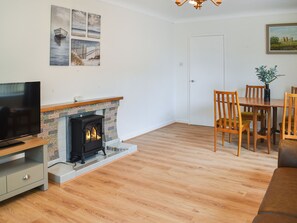 A living room with a fireplace, wooden flooring, a dining table with chairs, and a television on a stand. - 2 bedroom accommodation in Rhyl (Rhyl)