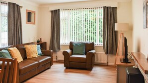 Ein Wohnzimmer mit braunem Ledersofa, einem braunen Sessel, einem Holztisch und einem Fernseher auf einem Standfuß.