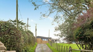 Un sendero rural que conduce a un edificio con fachada de madera y techo de metal, rodeado de vegetación y una valla de madera.