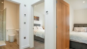 A hotel room with a wooden door, a bed with patterned bedding, a bedside table, and a wall-mounted light switch.