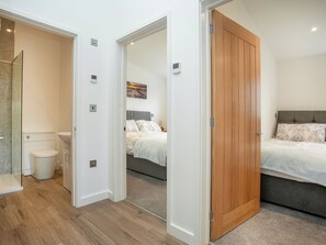 Habitación de hotel con puerta de madera, cama con ropa de cama estampada, mesita de noche y un interruptor de luz en la pared.