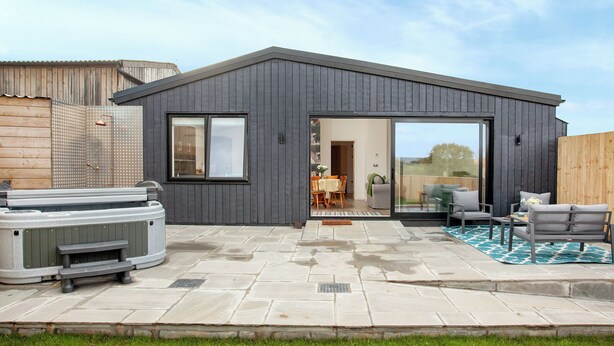 A modern house with a patio area, a hot tub, and a sliding glass door leading to an indoor space.