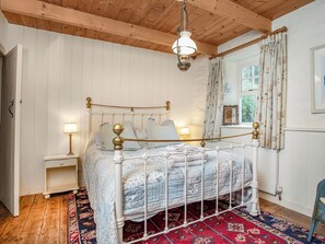 A bedroom with a wooden ceiling, a bed with a metal frame, a nightstand, a window with curtains, and a patterned rug. - 3 bedroom accommodation in Helston & The Lizard (The Lizard, near Falmouth)