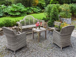 A garden with a wooden bench, wicker chairs, and a table with a vase of flowers.