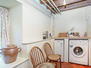 A compact kitchen with a washing machine, a small refrigerator, and a wooden chair.