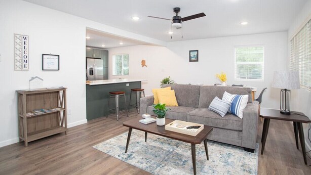 Ein modernes Wohnzimmer mit grauem Sofa, Couchtisch aus Holz und einer Küche im Hintergrund.
