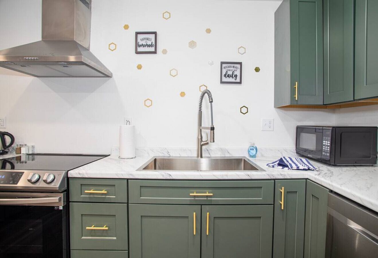 A kitchen with a stainless steel sink, a microwave, and green cabinets with gold handles.
