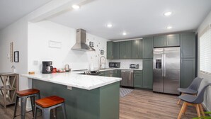 A modern kitchen with green cabinets, a stainless steel refrigerator, and a marble island with stools. - 3b2b newly remodeled modern Fairbanks house close to everything (Fairbanks)