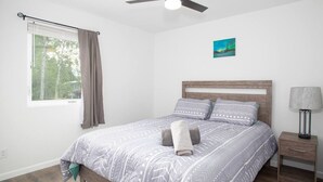 A bedroom with a bed, a nightstand, a ceiling fan, a window with curtains, and a painting on the wall. - 3b2b newly remodeled modern Fairbanks house close to everything (Fairbanks)