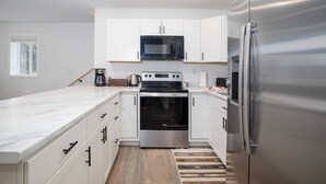 Eine moderne Küche mit weißen Schränken, einem Edelstahl-Kühlschrank, einer Mikrowelle, einem Backofen und einer Kaffeemaschine.