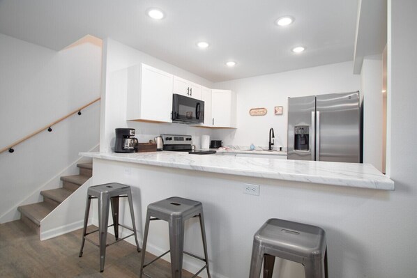 A modern kitchen with white cabinetry, stainless steel appliances, and a marble countertop.