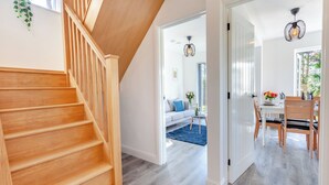 Ein modernes Interieur mit einer Holztreppe, einem Essbereich mit Tisch und Stühlen sowie einem Wohnzimmer mit Sofa und Couchtisch.