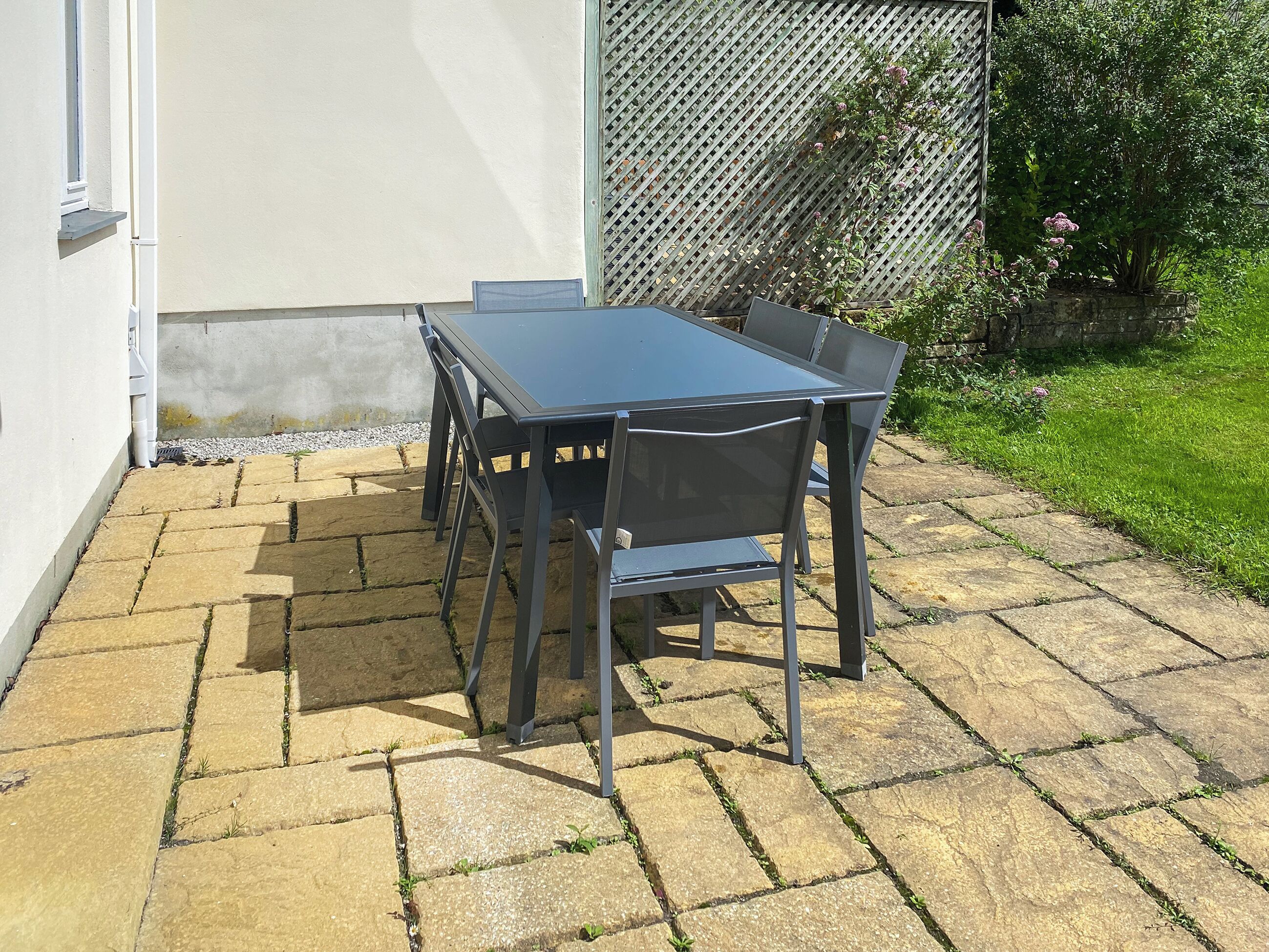 Une terrasse avec une table et des chaises, un sol en pierre et une clôture ornée de plantes.