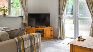 Un salon avec un téléviseur posé sur un meuble en bois, un canapé, une table basse et une fenêtre avec des rideaux.