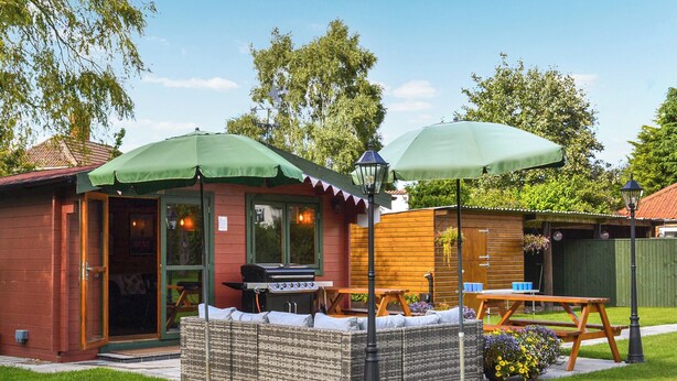 Une terrasse extérieure accueillante, dotée d’un barbecue, de deux parasols et d’une clôture en bois.