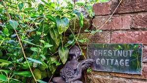 A garden area with a sign reading "Chestnut Cottage" and a bird statue. - 2 bedroom accommodation in Coxley Wick, near Wells (Coxley Wick, near Wells)