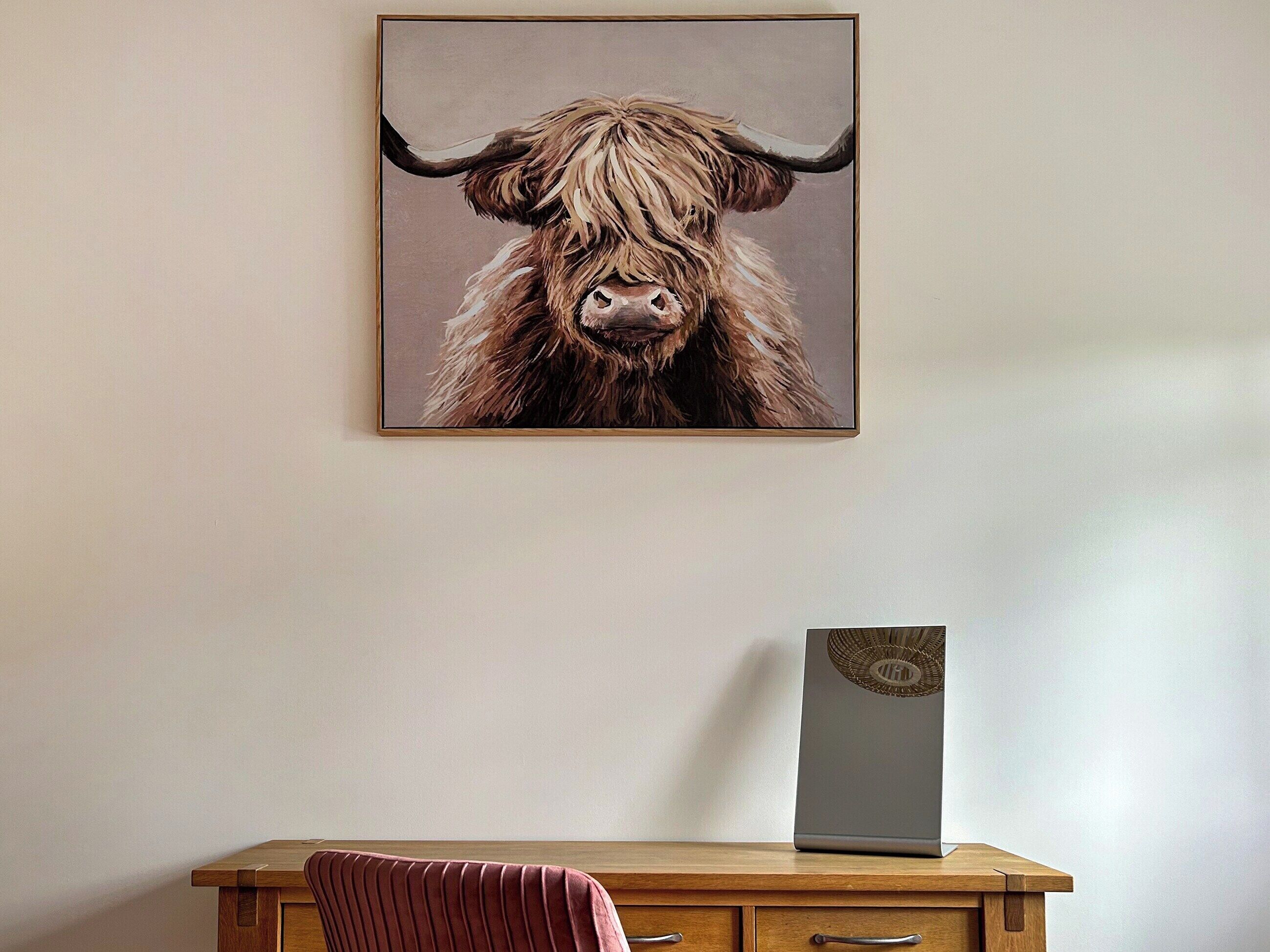 Ein gerahmtes Kunstwerk mit einem Jak auf einer Wand, ein Holztisch mit Schubladen und eine Vase mit dekorativem Deckel.