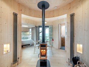 A wooden interior with a central wood stove, a bed, a dining area, and a bathroom.