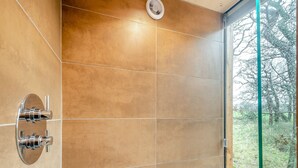Un baño con cabina de ducha de vidrio, grifo de pared y vistas a un bosque a través de la puerta de cristal.
