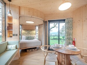 Et træinteriør med seng, siddeområde, spisebord og udsigt gennem et stort vindue.