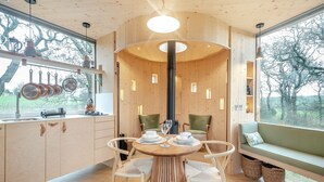 Una cocina moderna con armarios de madera, un comedor con mesa redonda y un amplio ventanal con vistas a árboles.