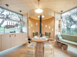 A modern kitchen with wooden cabinetry, a dining area with a round table, and a large window offering a view of trees.