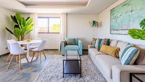 A modern living room with a dining area, a sofa, a coffee table, and a large abstract painting on the wall. - Falesia Beach C at Falesia Beach (Albufeira)