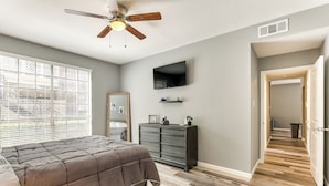 Una camera da letto con un letto, una ventola a soffitto, un comò, una TV e un corridoio con pavimento in legno.