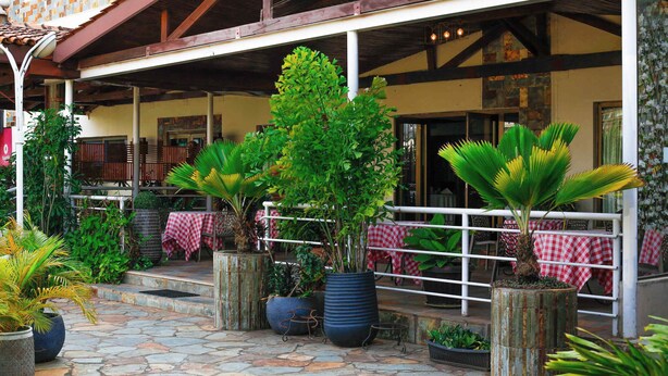 An outdoor patio area with stone flooring, potted plants, and a covered seating area with red and white checkered tablecloths. - Ave Maria Hotel (Accra)