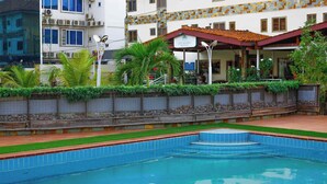 A swimming pool with a tiled edge, surrounded by a low wall with plants and a stone border. - Ave Maria Hotel (Accra)