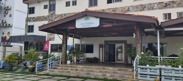 Exterior del Hotel Ave Maria con un acceso cubierto, escalones que conducen a la entrada y plantas en macetas alrededor del área.