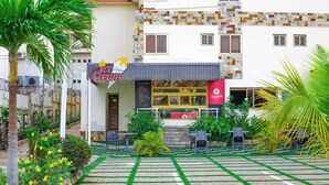 A restaurant with outdoor seating, a tiled patio, and a garden area with palm trees and flowers. - Ave Maria Hotel (Accra)